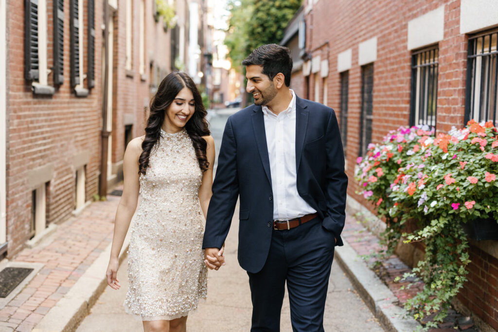 A couple dressed in evening wear stroll through a narrow alley, with the woman in a sparkling gold dress, radiating glamour and happiness in an intimate urban setting