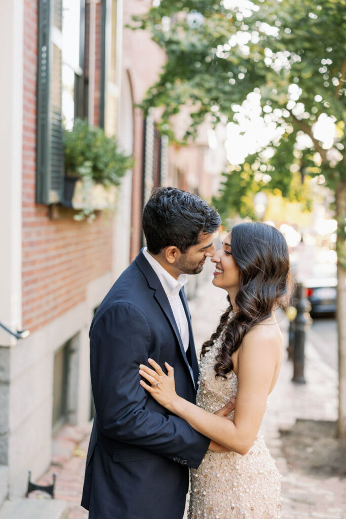 A romantic close-up of a couple embracing on a city street, surrounded by the greenery of trees and brick buildings, sharing a tender and private moment