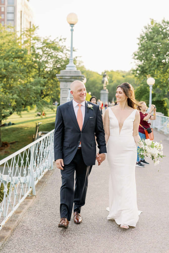A couple walks hand-in-hand down a garden path in the Boston Public Garden, surrounded by vibrant flowers and greenery, symbolizing a romantic walk.