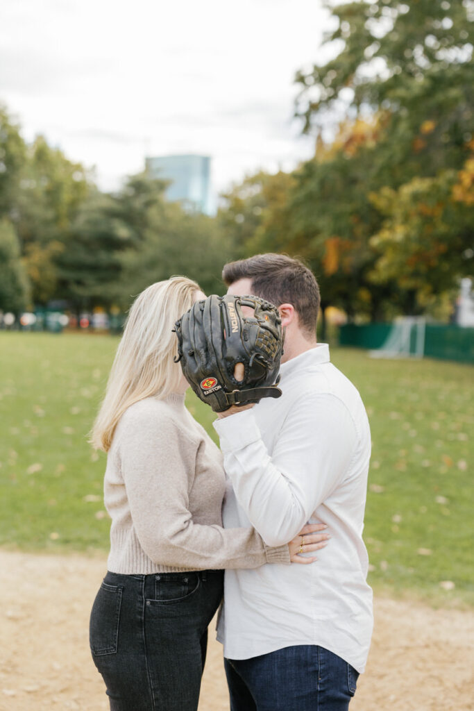 A playful couple where the man covers their faces with a baseball glove, creating a sense of fun and closeness.