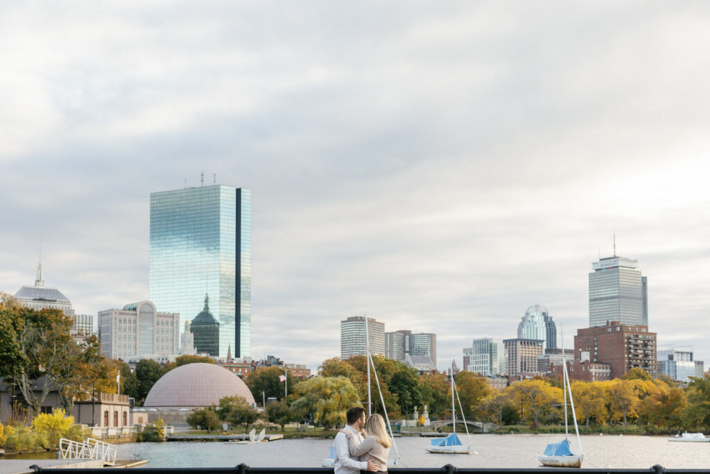 A tender embrace captured between a couple, the city’s reflective buildings towering in the distance, under a clear sky.
