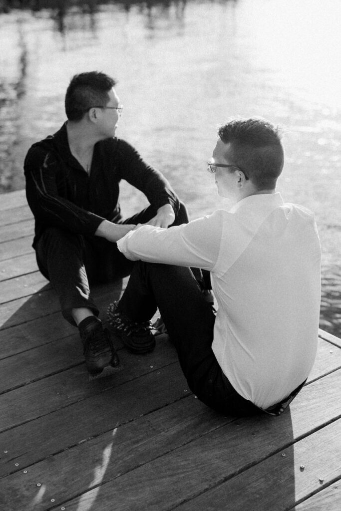 A serene moment between a couple sitting on a wooden dock, one with his arm around the other.