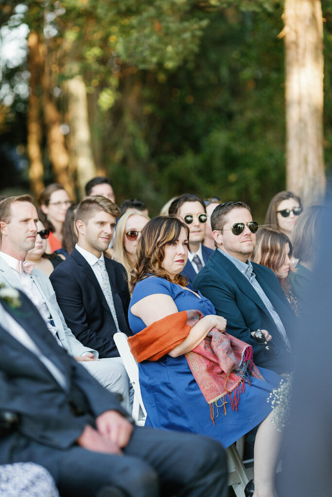 Guests seated in rows at an outdoor wedding ceremony, attentively watching the proceedings.