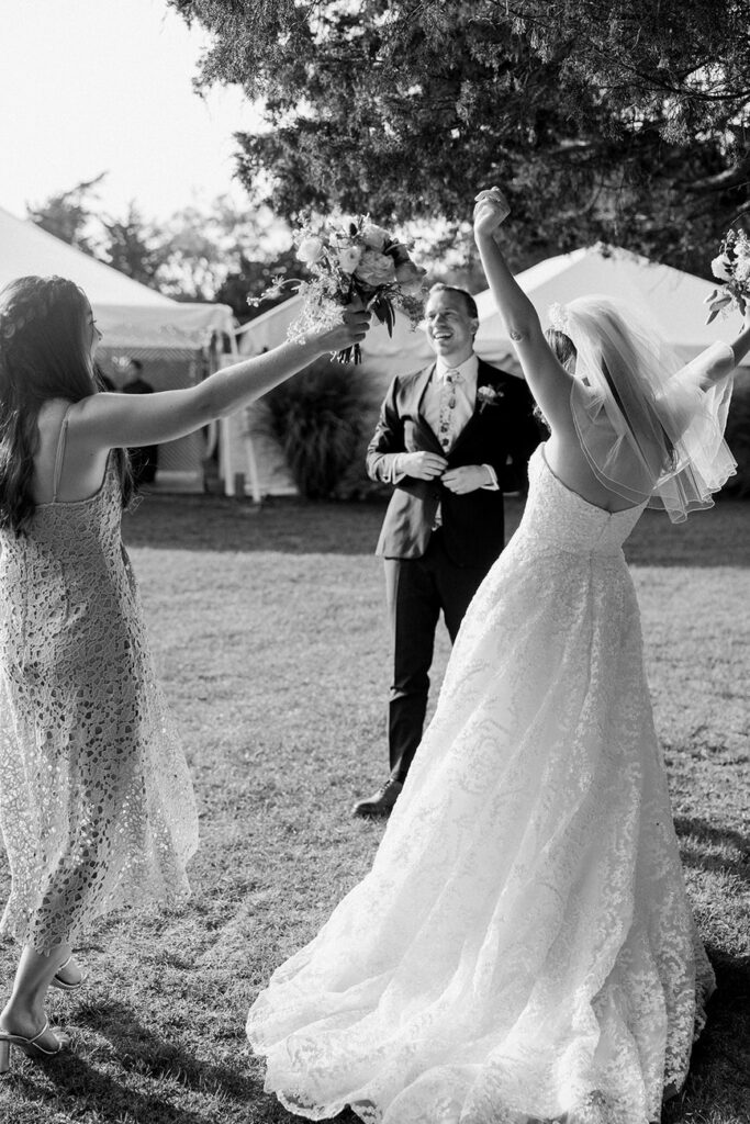 A celebratory moment with a bride throwing her bouquet towards a group, with the groom cheering beside her in a black and white photo.
