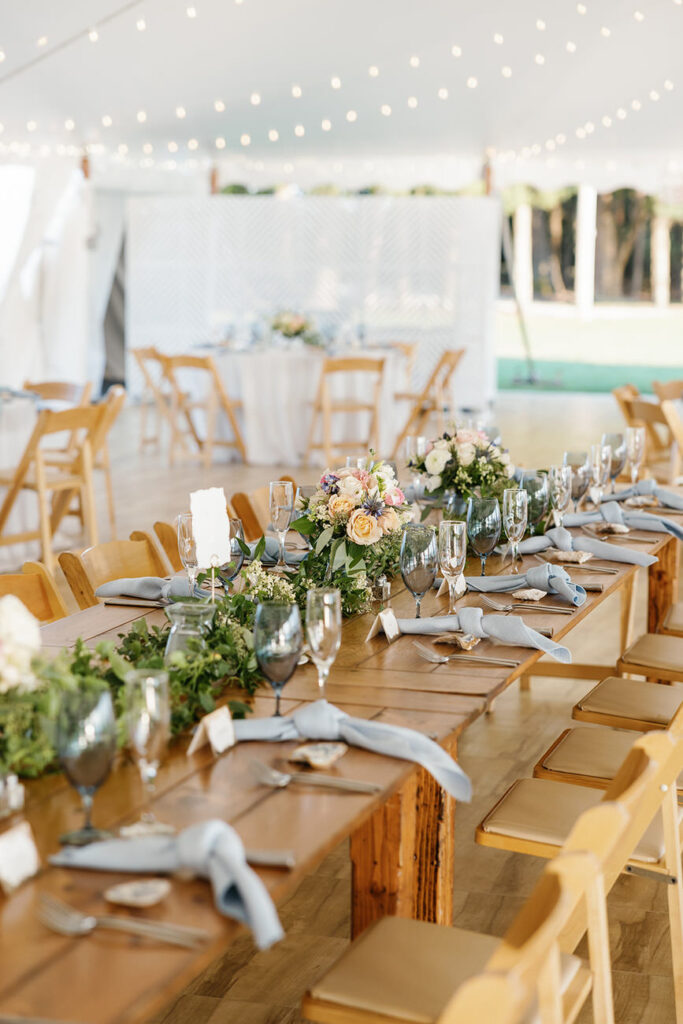 A beautifully arranged wedding reception table set with wooden chairs, floral centerpieces, and elegant place settings, under string lights.