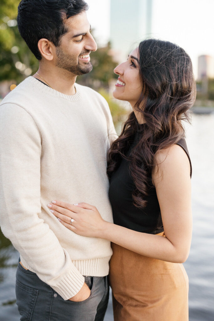 An affectionate moment captured as a couple gazes into each other's eyes, with the Charles River and Boston skyline providing a picturesque backdrop.