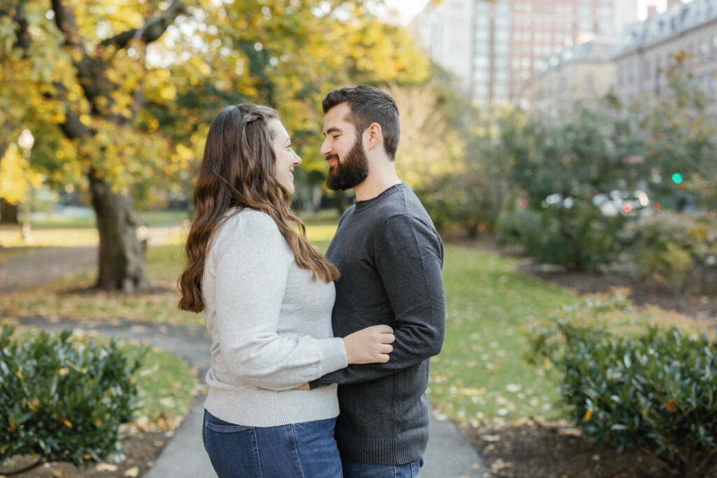 A couple with their arms around each other smiling while standing in a park
