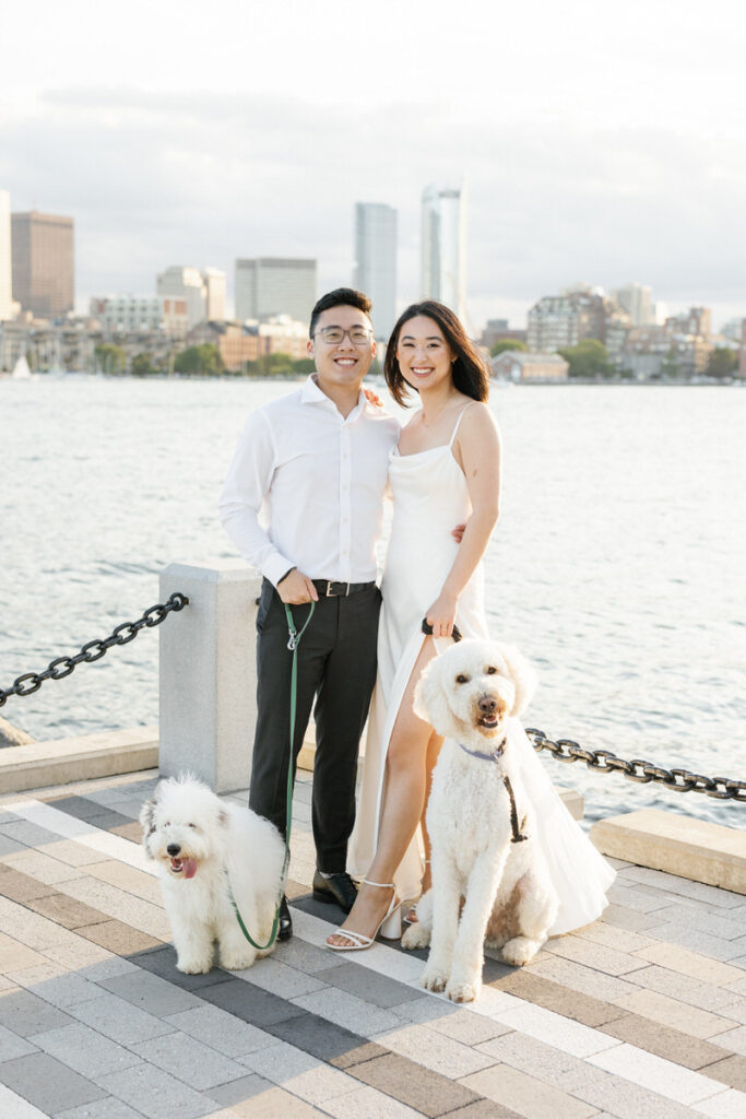 A couple with two dogs sitting at their feet as they smile. 
