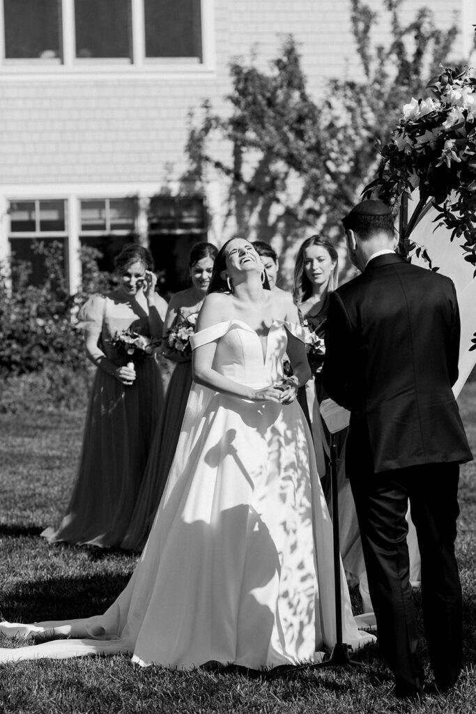 Bride laughing with head back as groom reads vows