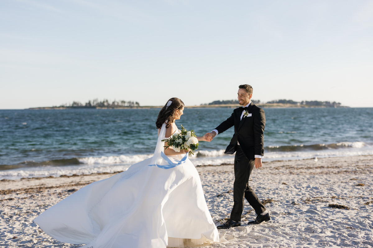Bride and groom holding hands on a beach, looking at each other with the ocean in the background during their Inn by the Sea wedding