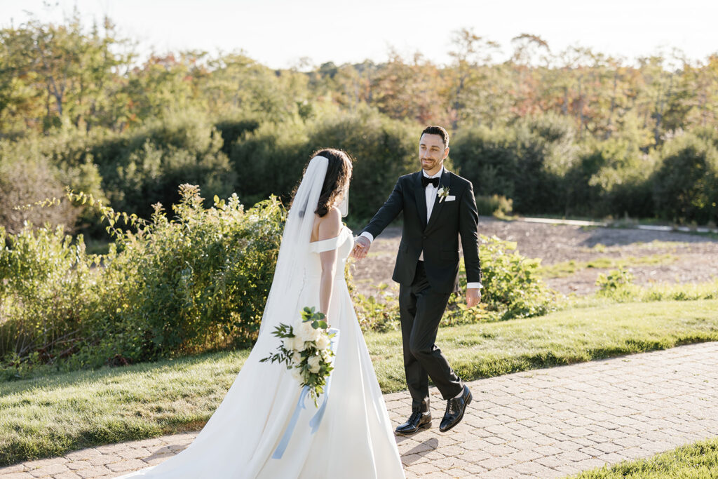 Newlywed couple playfully walking on a stone path, groom holding the bride's hand and walking backwards looking at her
