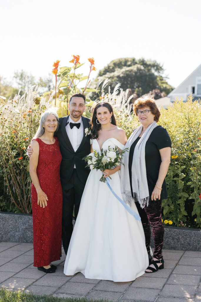 Bride and groom with two family members, standing in a garden with colorful flowers