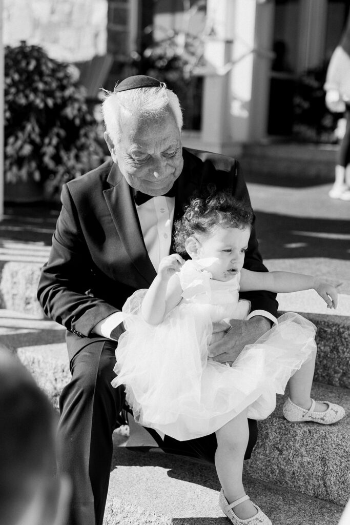 Man in a suit sitting on the stairs with the flower girl in a dress