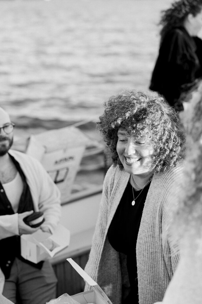 Happy woman smiling on a sailboat, wearing a sweater with her curly hair blowing in the wind