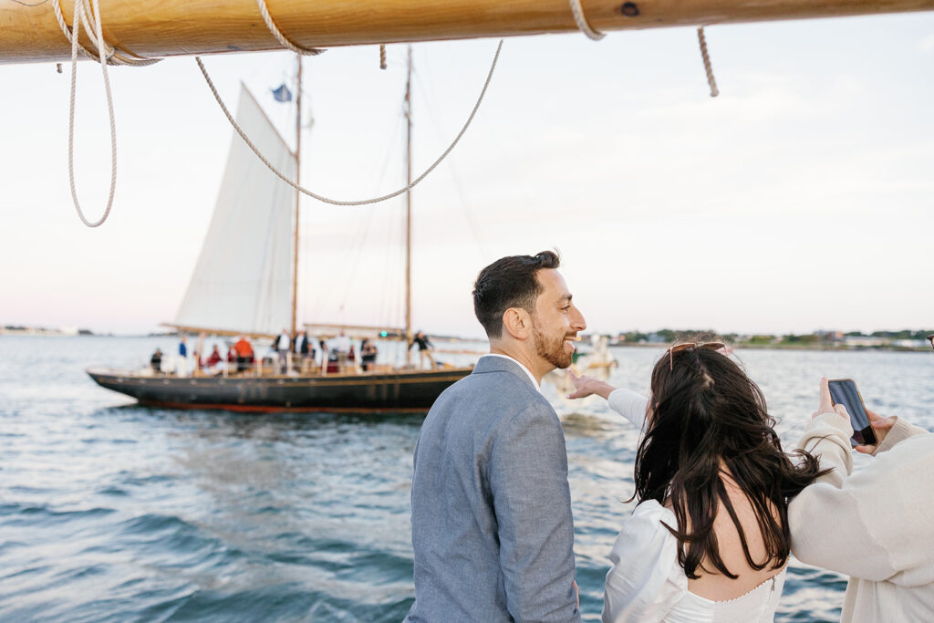 A woman and man looking out at a sailboat filled with people on the ocean.