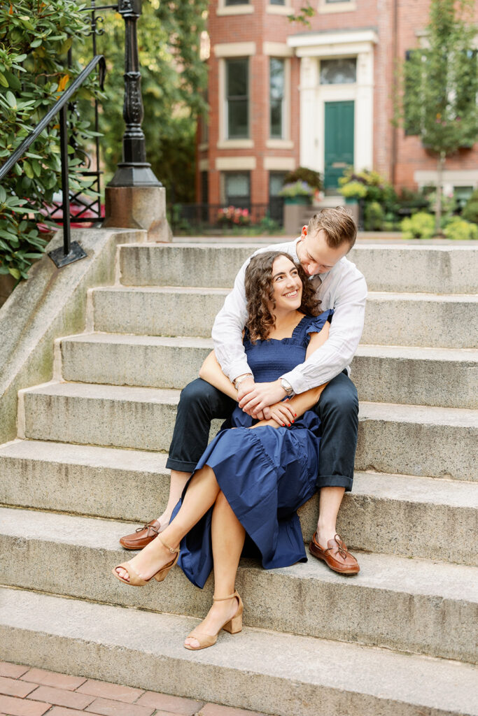 A couple embracing and smiling up at each other while sitting on steps.