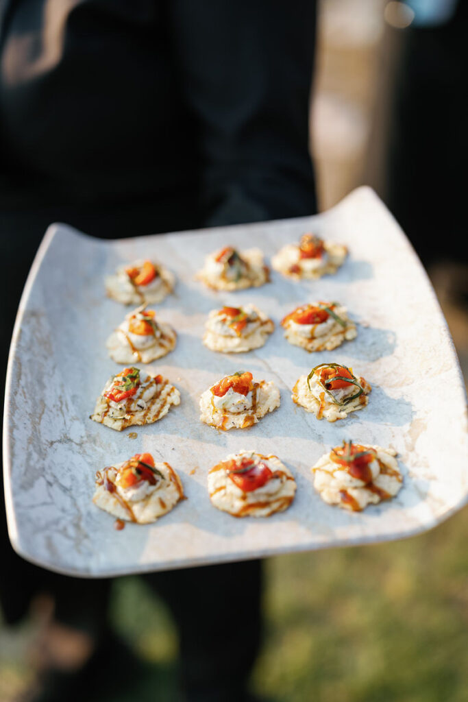 An appetizer platter held by a server, presenting small savory bites garnished with herbs and tomato on a white and blue marbled plate