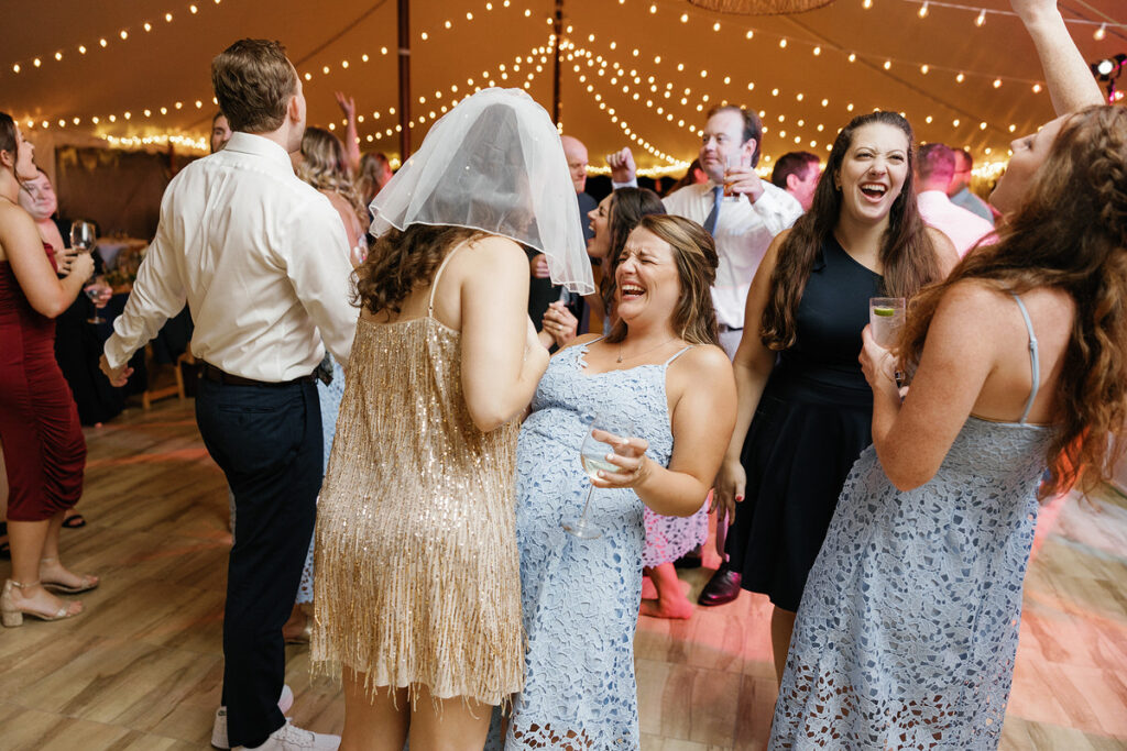 Bride in a wedding dress and veil laughing heartily with guests during a dance
