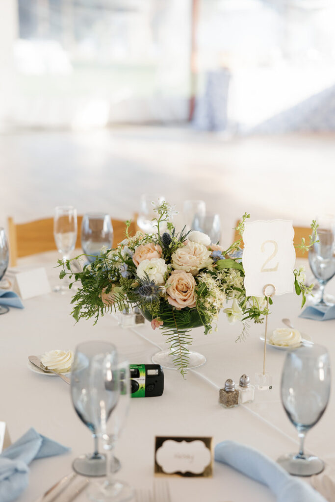 Elegant wedding table setting with a floral centerpiece featuring roses and greenery, alongside clear glassware