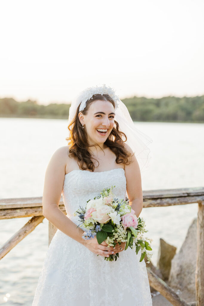 A beaming bride in a strapless white gown smiles joyously while the holding a bouquet of flowers.