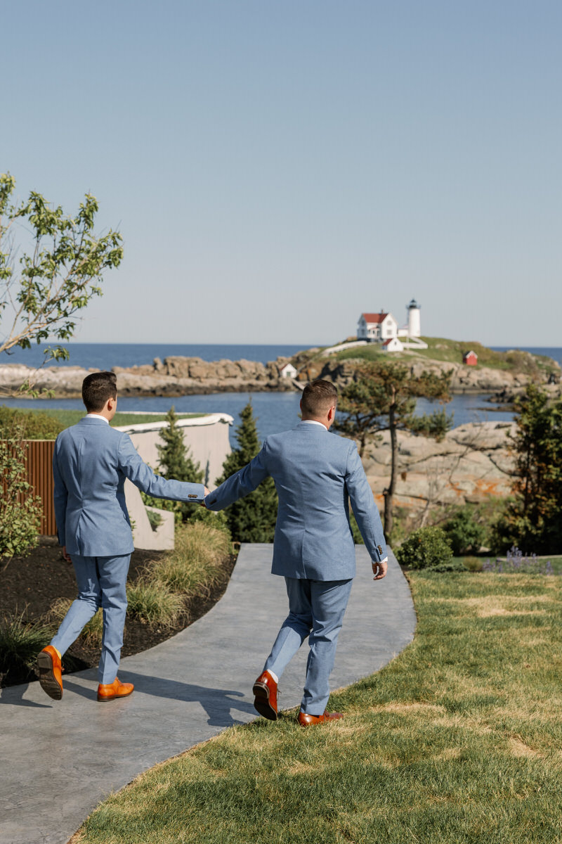 Two grooms walking hand in hand towards a lighthouse