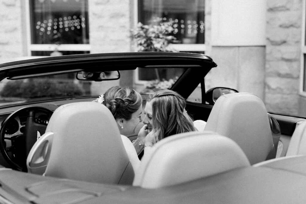 Two brides smile at each other in a car