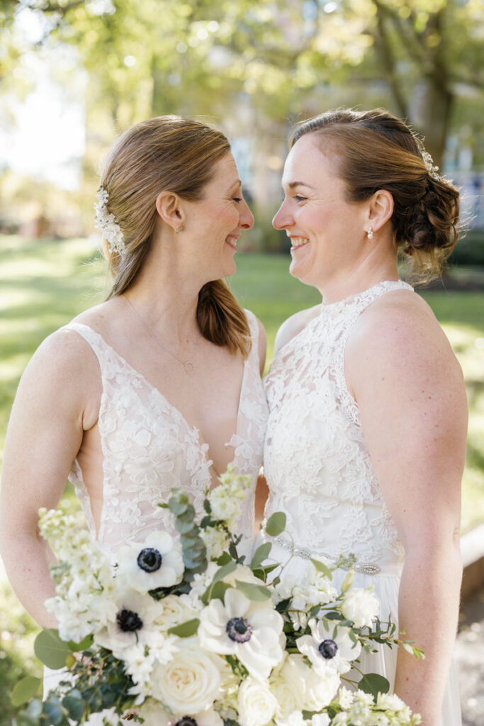 Two brides with their arms around each other smiling together. 