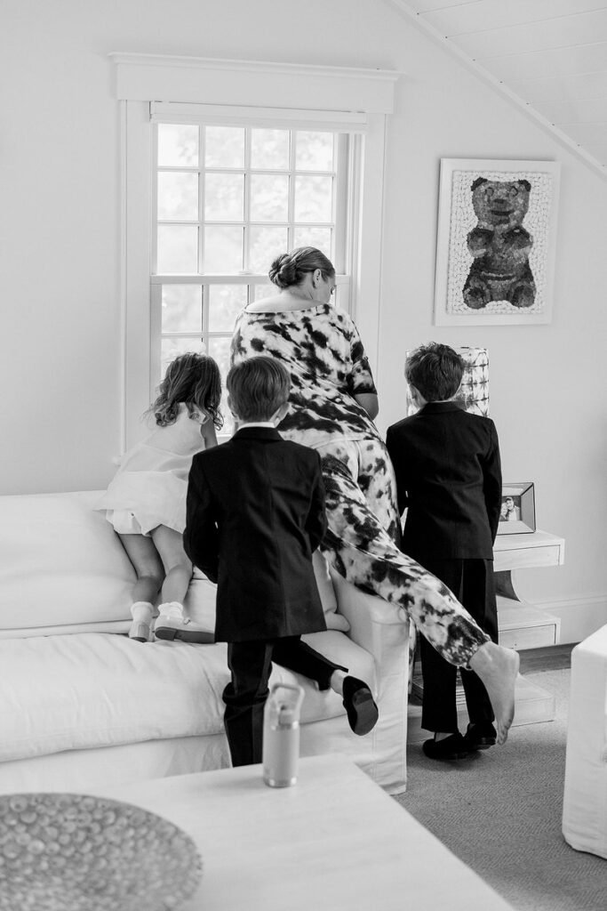 A person and three kids leaning on a couch looking out a window. 