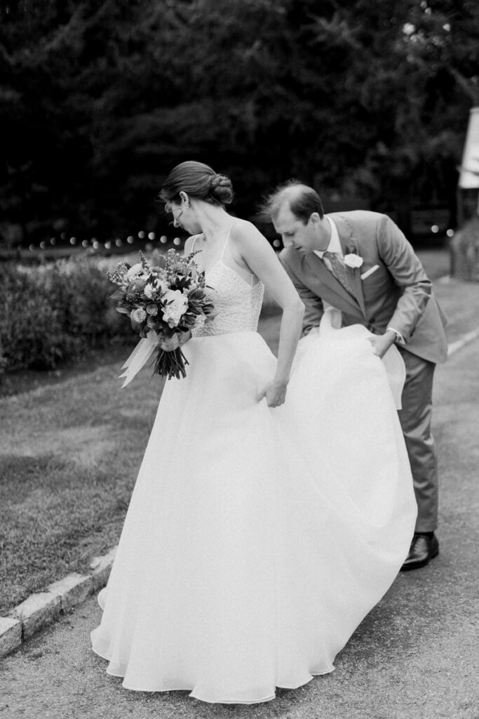 A groom helping a bride adjust the back of her dress. 