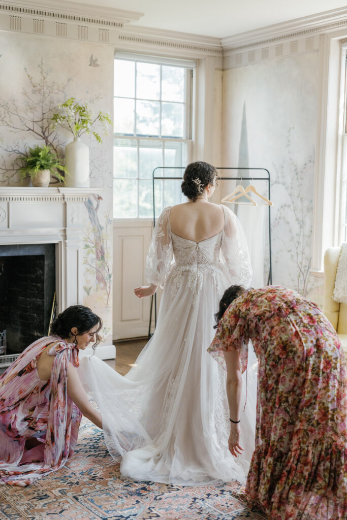 Two bridesmaids place the bride's train as she puts on the dress for the first time. 